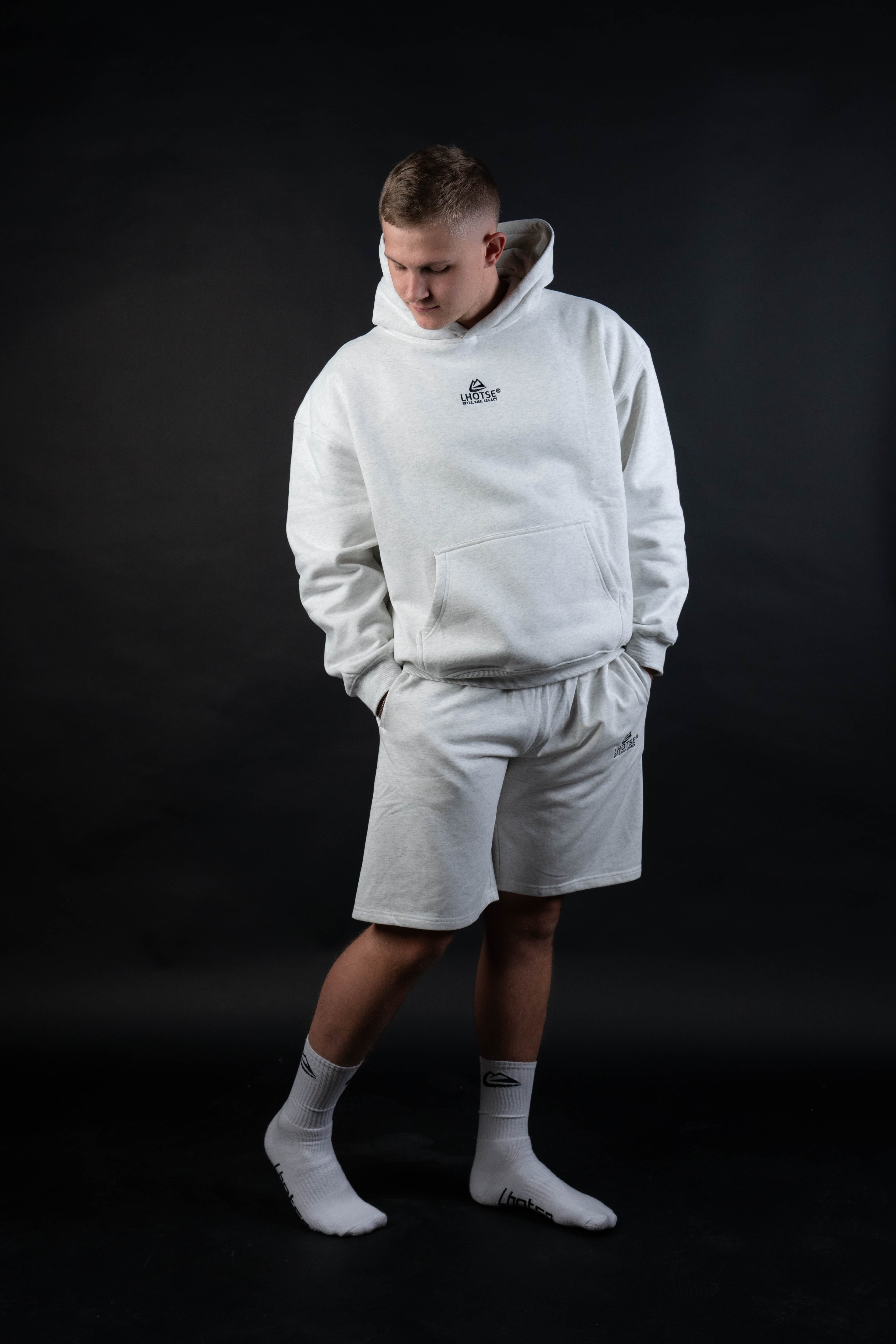 Person wearing a gray hoodie and shorts set on a black background
