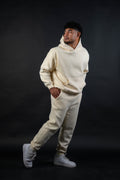 Person wearing a beige hoodie and pants set on a black background