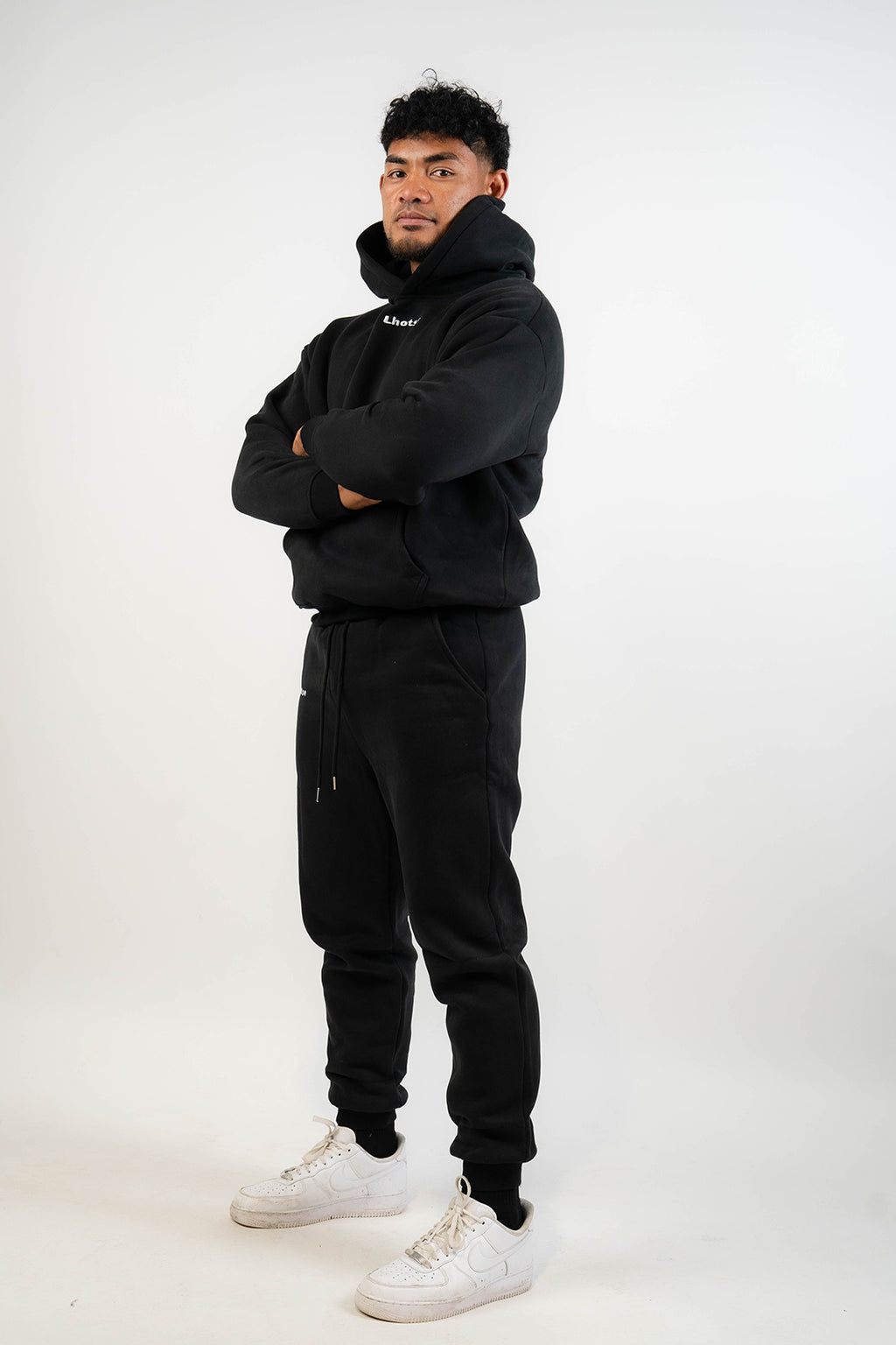 Person wearing a black hoodie and black pants with white sneakers on a white background