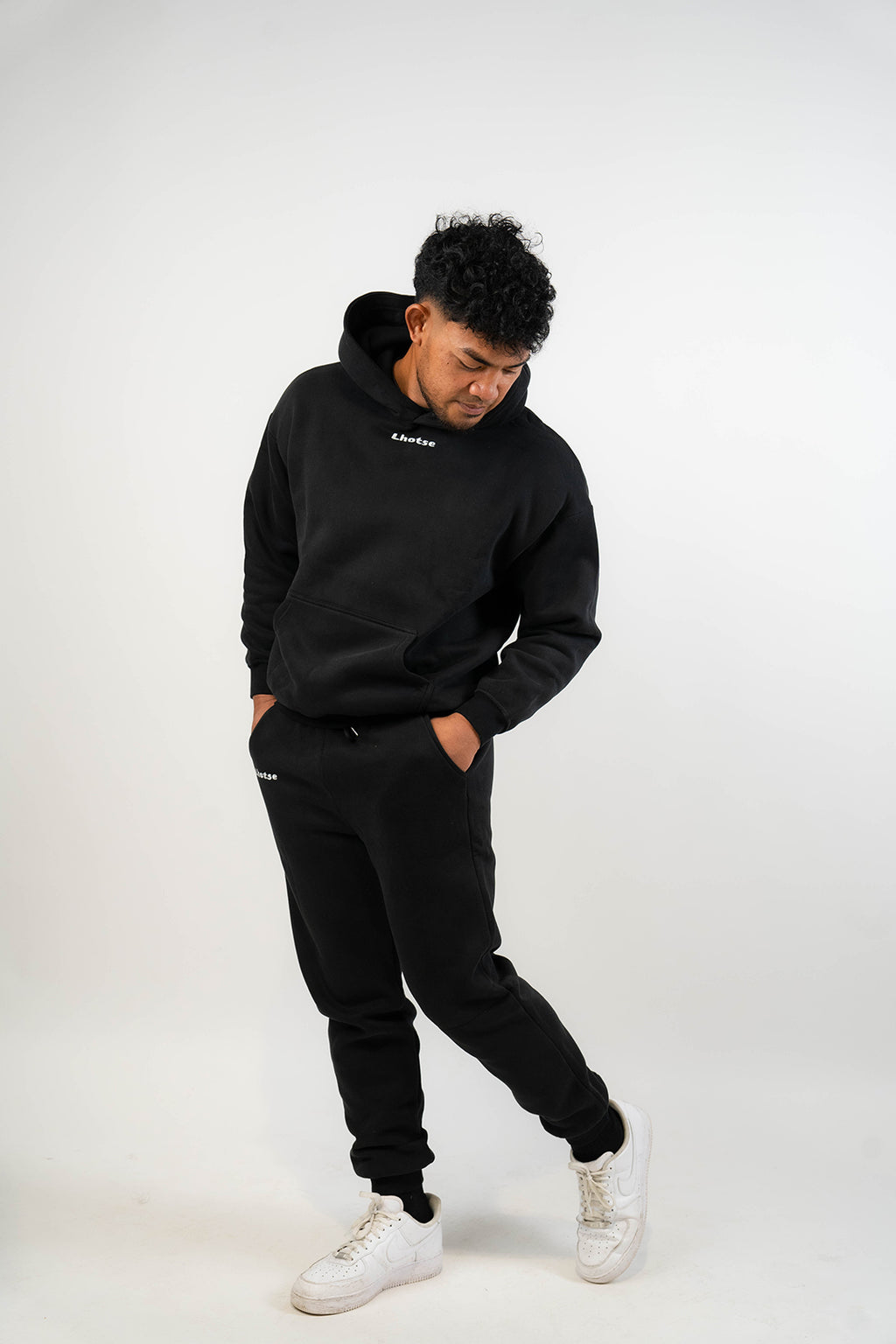 Person wearing a black hoodie and pants with white sneakers on a white background